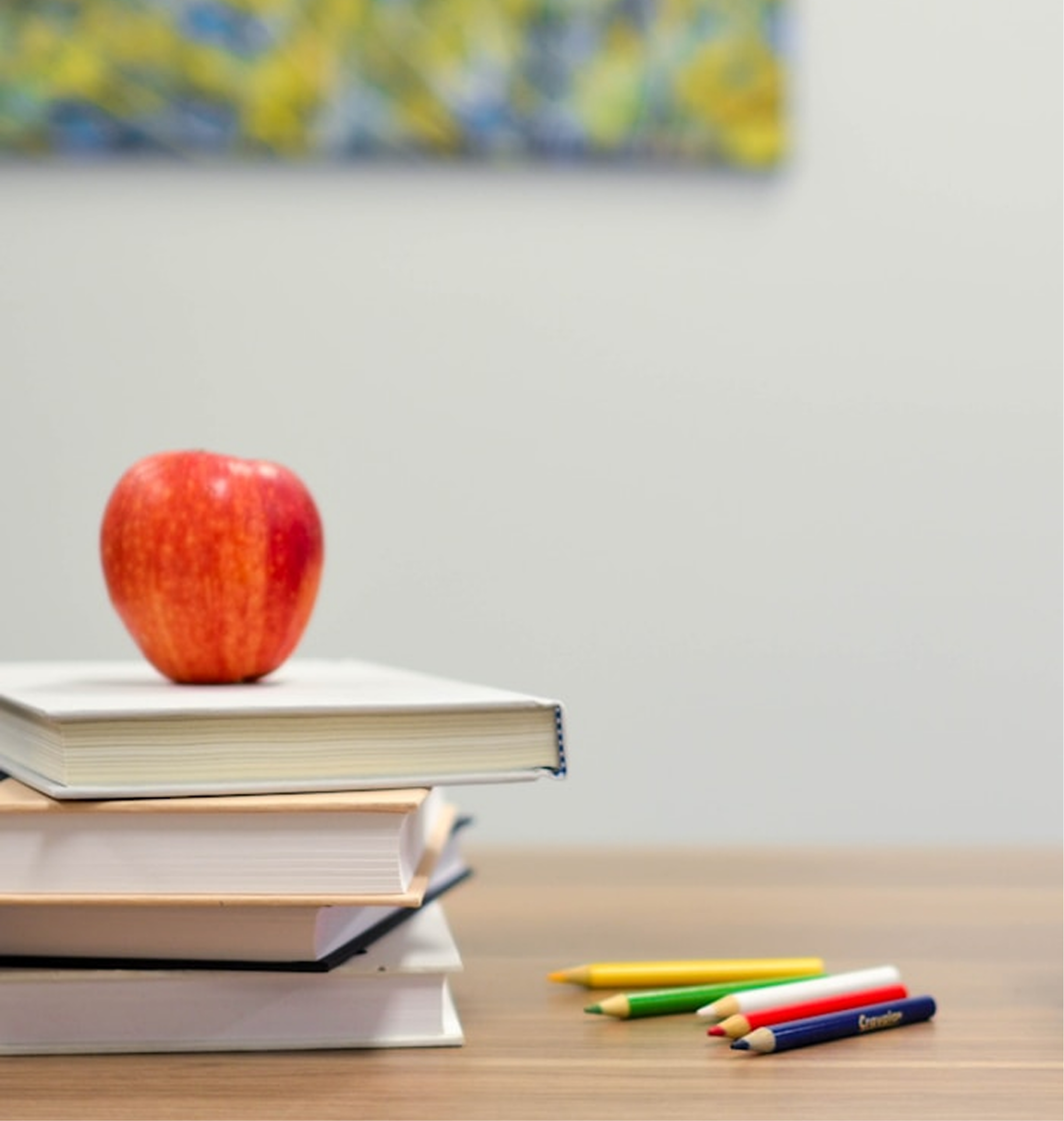 Books stacked on a desk with an apple and coloured pencils